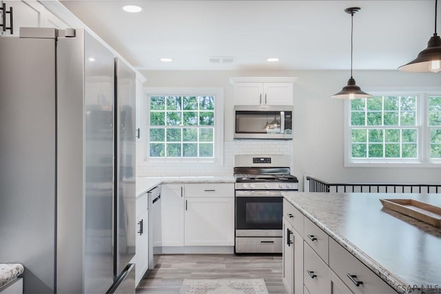 kitchen featuring white cabinetry, tasteful backsplash, hanging light fixtures, light wood-type flooring, and stainless steel appliances