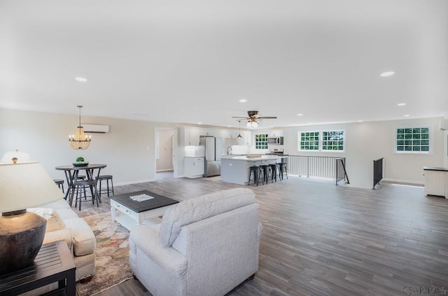 living room with wood-type flooring, ceiling fan with notable chandelier, and a wall mounted air conditioner