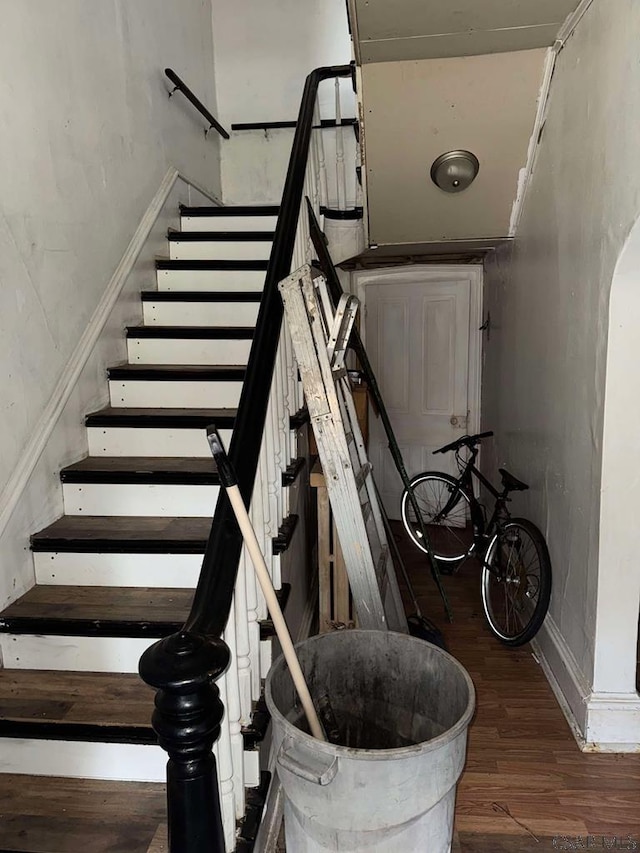 staircase featuring arched walkways and wood finished floors