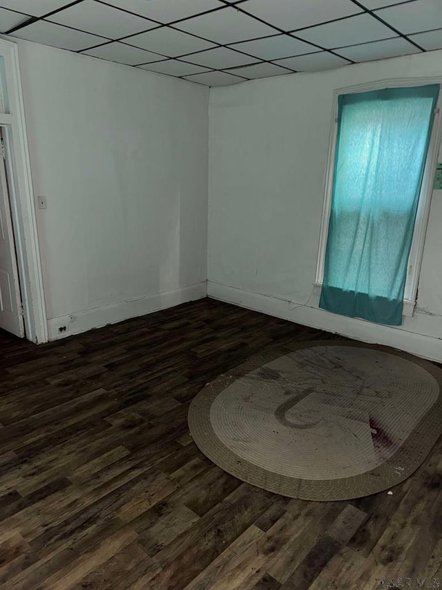 empty room with dark wood-type flooring, a drop ceiling, and baseboards