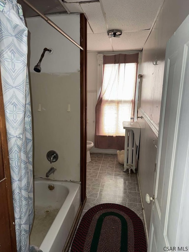 bathroom with toilet, shower / tub combo with curtain, a drop ceiling, and wainscoting