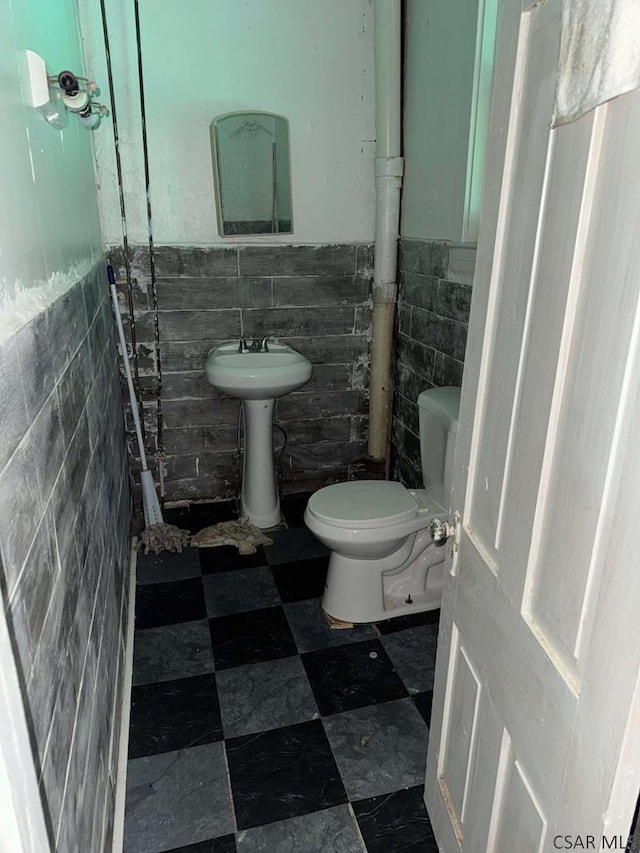 half bath with wainscoting, toilet, and tile walls