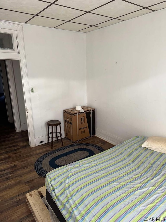 bedroom featuring baseboards, a drop ceiling, and wood finished floors