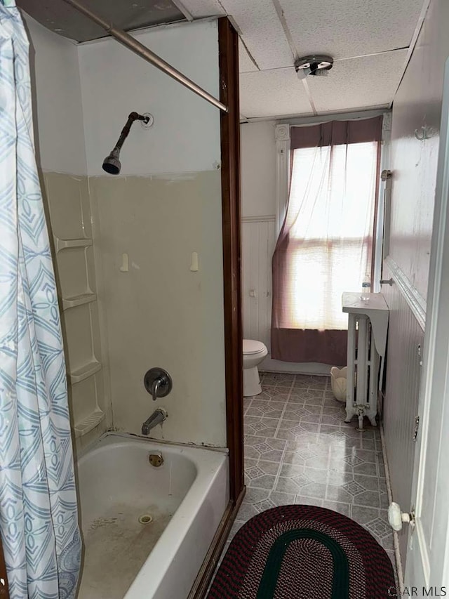 bathroom with a paneled ceiling, a wainscoted wall, toilet, and shower / bath combo