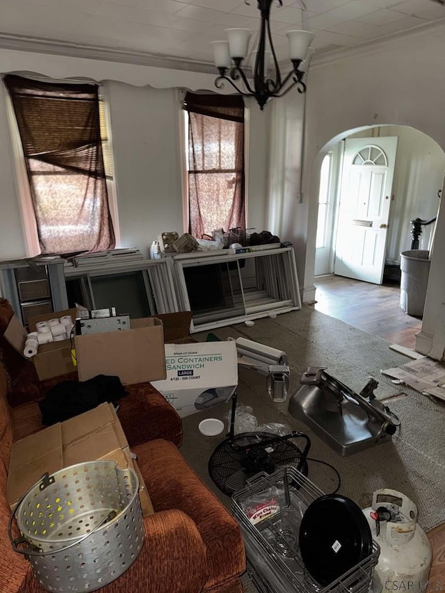 living area featuring crown molding, arched walkways, a notable chandelier, and wood finished floors