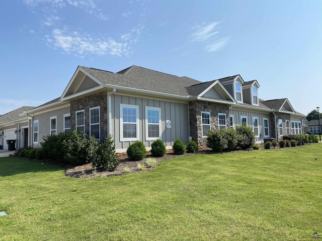 view of front facade with an attached garage, stone siding, roof with shingles, a front lawn, and board and batten siding