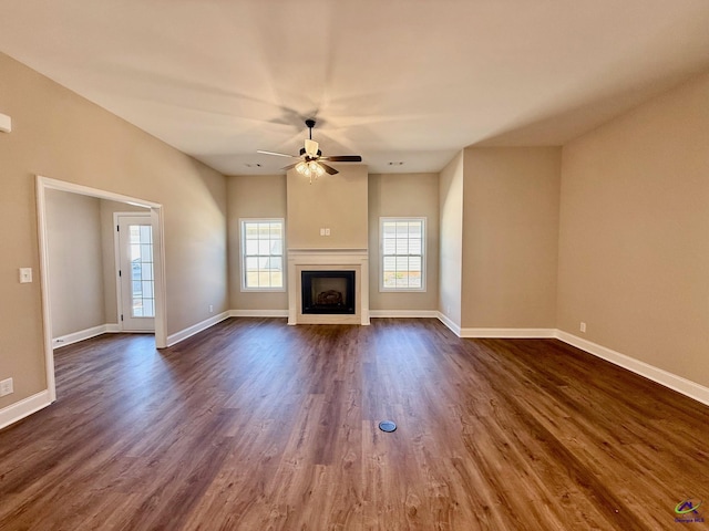 unfurnished living room with a fireplace, dark wood finished floors, a ceiling fan, and baseboards