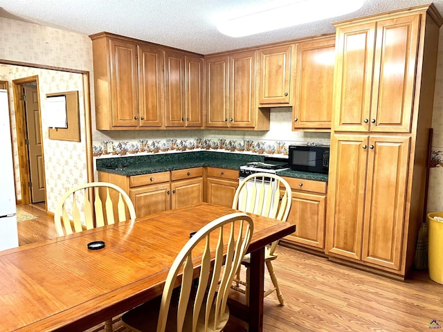 2382 Gallimore Mill Rd, Jeffersonville, GA 31044 - kitchen featuring wallpapered walls, black microwave, light wood-type flooring, dark countertops, and a textured ceiling