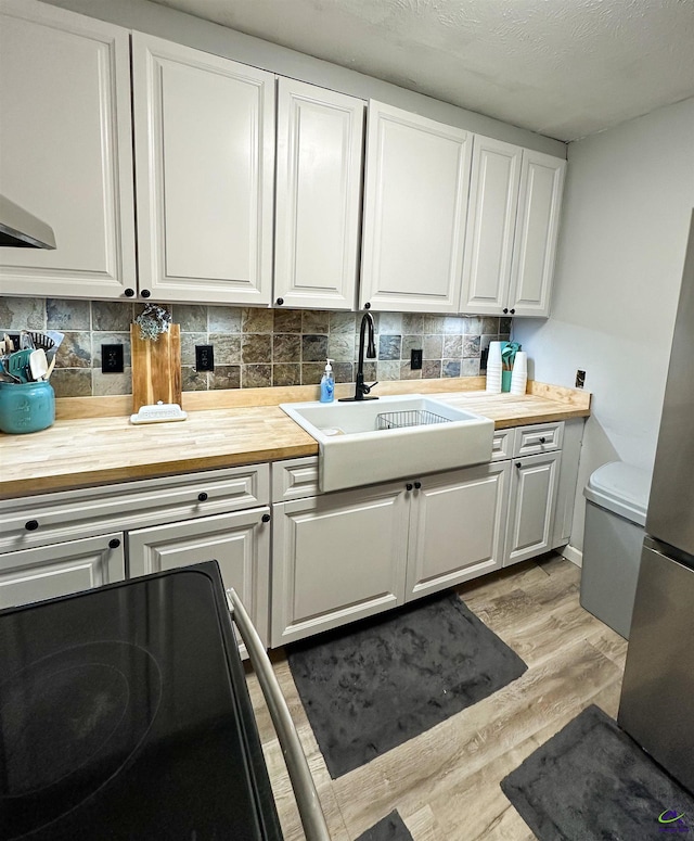 kitchen with sink, tasteful backsplash, white cabinetry, and light hardwood / wood-style floors