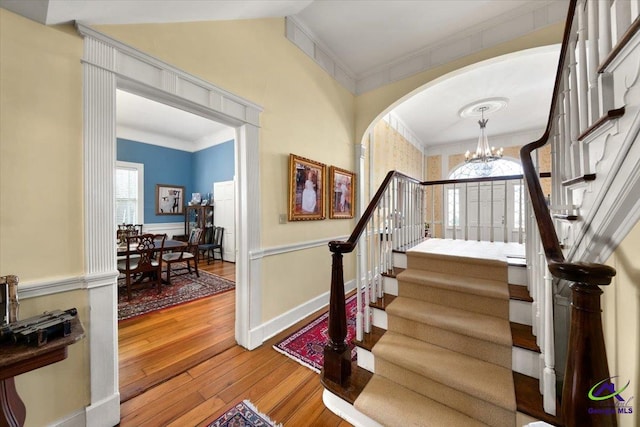 stairway with an inviting chandelier, crown molding, and hardwood / wood-style flooring