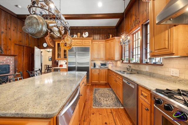 kitchen featuring premium appliances, light hardwood / wood-style floors, sink, light stone counters, and wall chimney exhaust hood