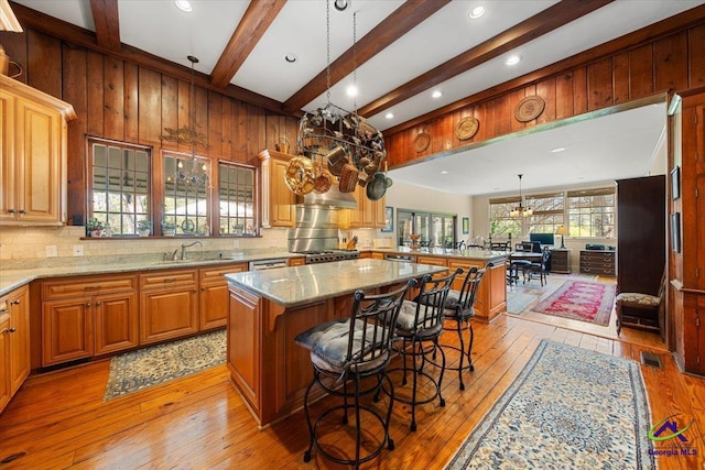 kitchen with sink, a kitchen island, a breakfast bar, light stone countertops, and light wood-type flooring