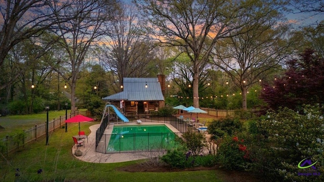 pool at dusk featuring a water slide and a lawn