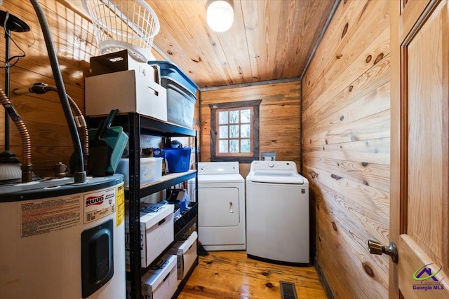 laundry area with electric water heater, wood walls, light hardwood / wood-style floors, and washing machine and dryer