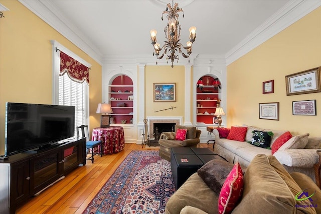 living room featuring ornamental molding, light hardwood / wood-style floors, a notable chandelier, and built in features