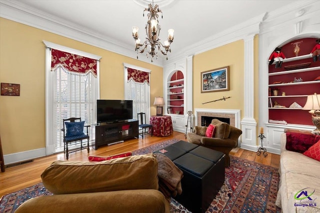 living room with built in features, crown molding, light wood-type flooring, and a chandelier