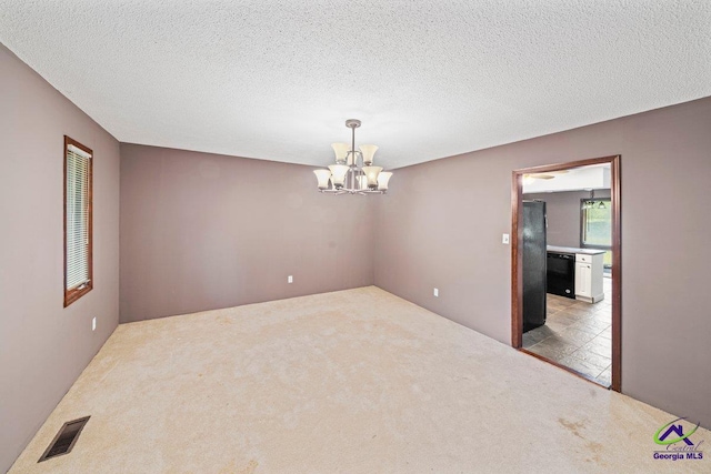 carpeted empty room with a textured ceiling and a chandelier