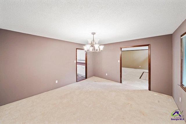 carpeted spare room featuring a chandelier and a textured ceiling