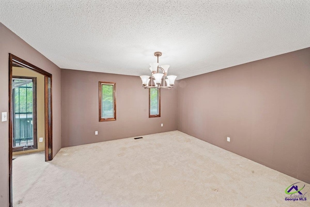 carpeted empty room with a notable chandelier and a textured ceiling