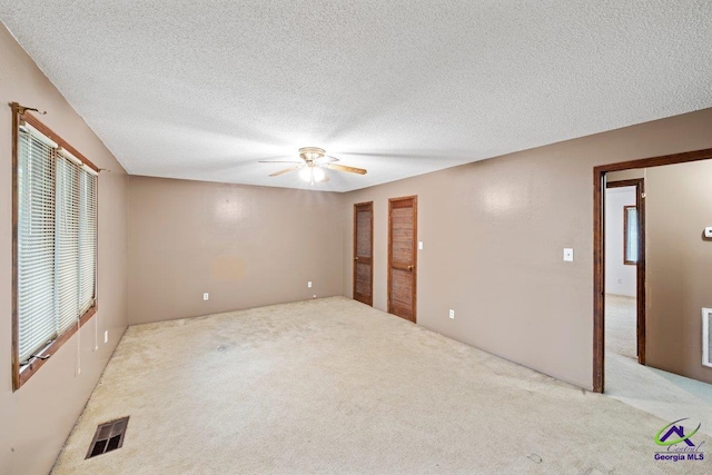 unfurnished room with ceiling fan, a textured ceiling, and light colored carpet