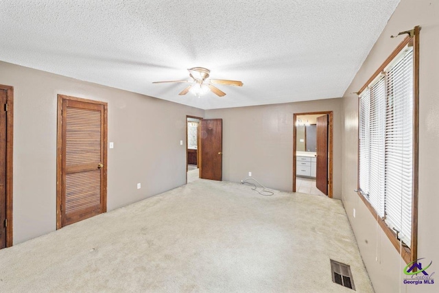 unfurnished bedroom with ceiling fan, ensuite bathroom, light colored carpet, and multiple windows