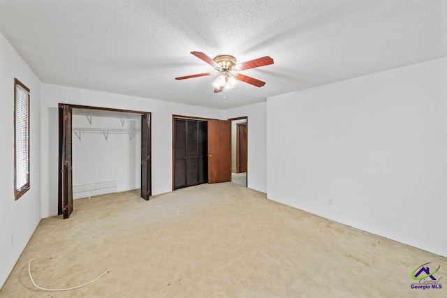 unfurnished bedroom featuring light carpet, two closets, ceiling fan, and a textured ceiling