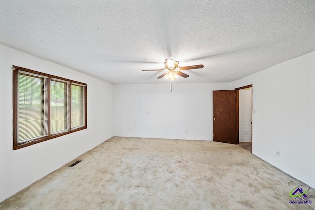 spare room featuring ceiling fan, light carpet, and a textured ceiling