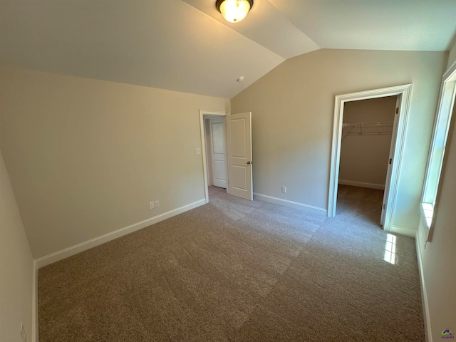 unfurnished bedroom featuring vaulted ceiling, a walk in closet, carpet floors, and a closet