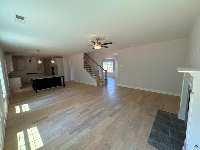 unfurnished living room with ceiling fan, light hardwood / wood-style floors, sink, and a fireplace