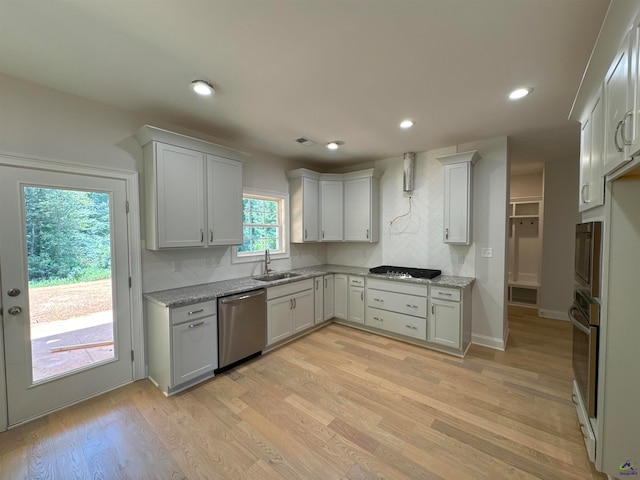 kitchen with decorative backsplash, stainless steel appliances, sink, light hardwood / wood-style floors, and white cabinetry