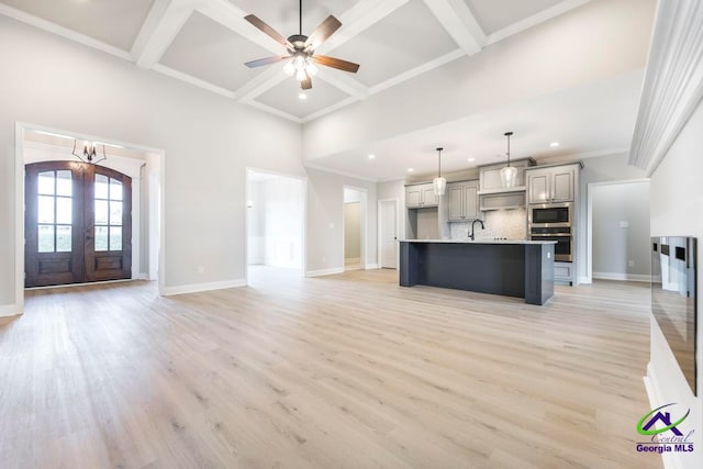 kitchen with french doors, a kitchen island with sink, appliances with stainless steel finishes, hanging light fixtures, and light hardwood / wood-style flooring