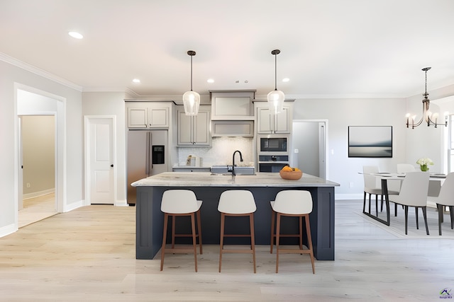 kitchen featuring stainless steel appliances, light hardwood / wood-style floors, sink, an island with sink, and decorative light fixtures