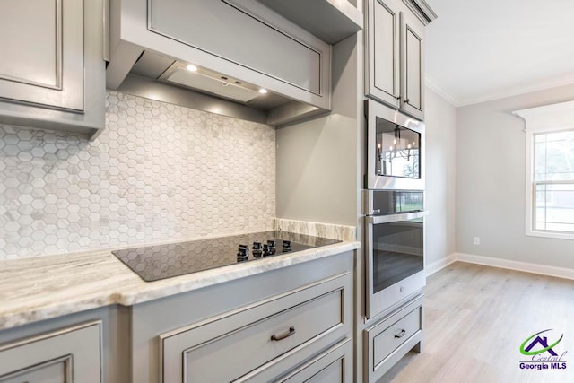 kitchen with light stone counters, ornamental molding, tasteful backsplash, black electric stovetop, and light wood-type flooring