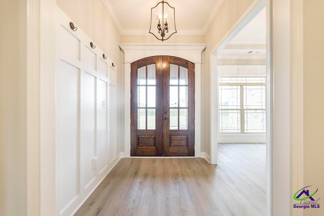 foyer entrance featuring a notable chandelier, light wood-type flooring, french doors, and ornamental molding