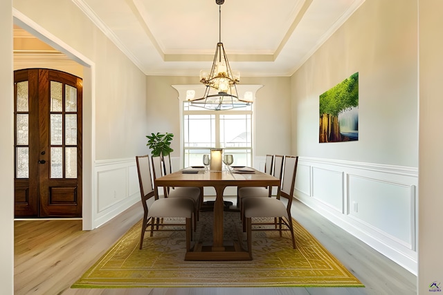 dining room featuring wood-type flooring, french doors, ornamental molding, a notable chandelier, and a raised ceiling