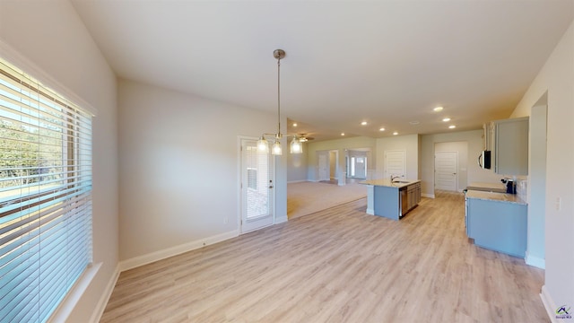 kitchen featuring a wealth of natural light, an island with sink, light wood-type flooring, and pendant lighting