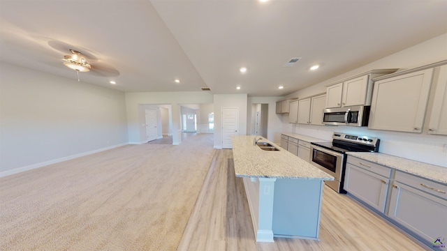 kitchen with a center island with sink, appliances with stainless steel finishes, sink, ceiling fan, and light colored carpet