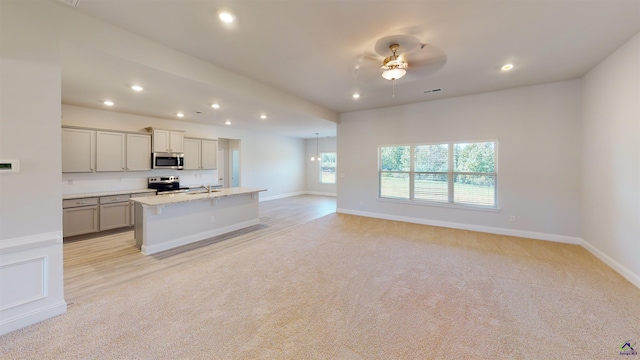 kitchen with stainless steel appliances, ceiling fan, an island with sink, gray cabinets, and light colored carpet