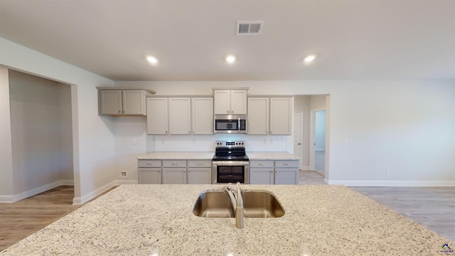 kitchen with light hardwood / wood-style floors, gray cabinets, light stone counters, sink, and appliances with stainless steel finishes