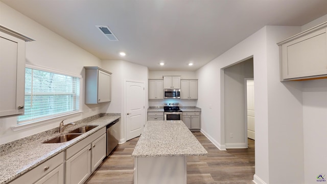 kitchen featuring wood-type flooring, appliances with stainless steel finishes, sink, light stone countertops, and a center island