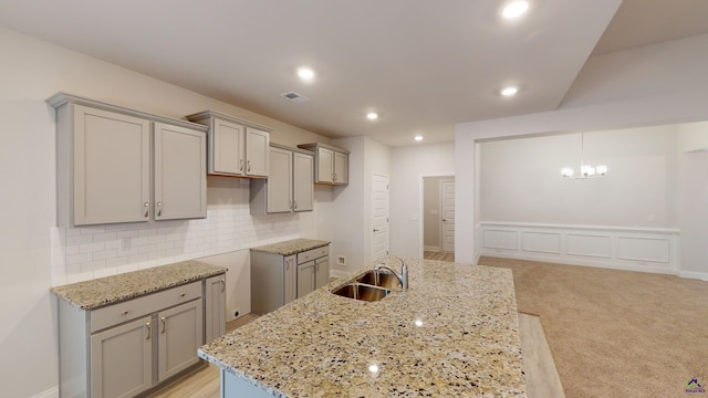 kitchen featuring light carpet, sink, decorative light fixtures, light stone counters, and a kitchen island