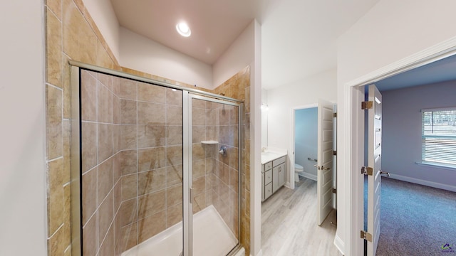 bathroom with hardwood / wood-style floors, toilet, a shower with shower door, and vanity