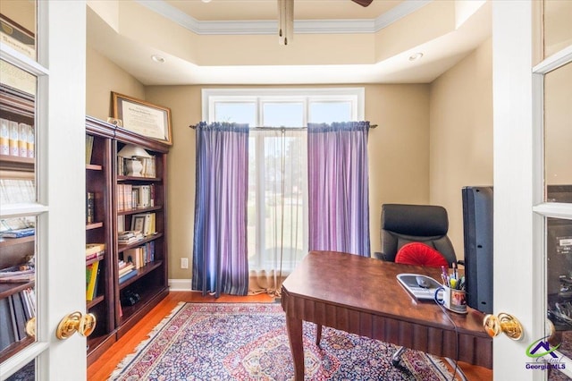 home office with wood-type flooring, ornamental molding, and a raised ceiling