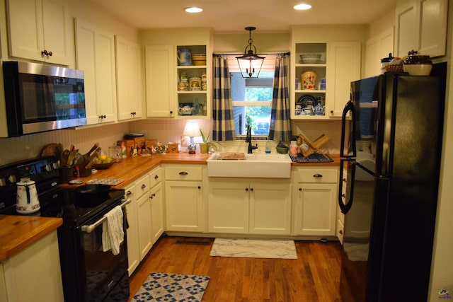 kitchen featuring butcher block counters, white cabinets, black appliances, pendant lighting, and sink