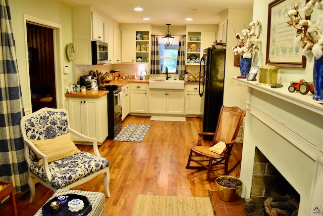 kitchen with white cabinets, electric range oven, sink, light wood-type flooring, and black fridge