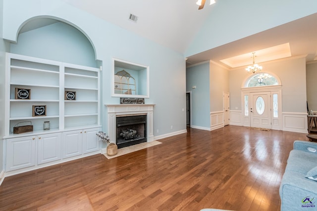 unfurnished living room featuring a notable chandelier, wood-type flooring, high vaulted ceiling, crown molding, and built in shelves