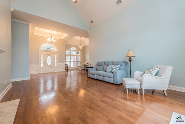 living room featuring hardwood / wood-style flooring, a high ceiling, a raised ceiling, and an inviting chandelier