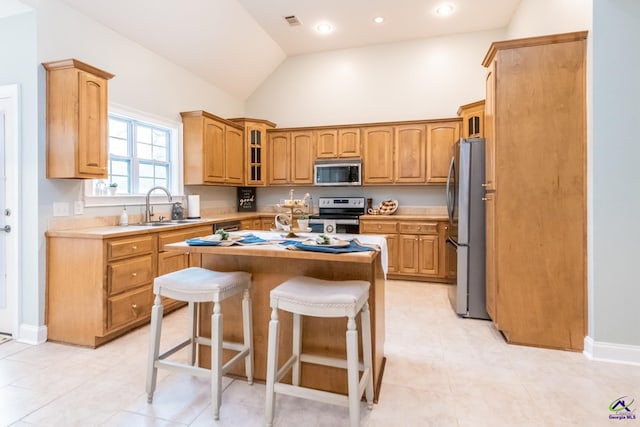 kitchen with a breakfast bar area, stainless steel appliances, vaulted ceiling, a kitchen island, and sink