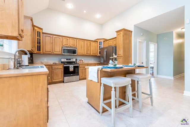 kitchen featuring a kitchen island, a breakfast bar, sink, a high ceiling, and appliances with stainless steel finishes