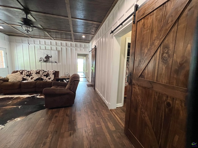 living room with wood walls, dark hardwood / wood-style floors, ceiling fan, and a barn door